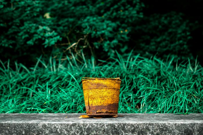 A yellow bucket sat beside a pond and greenery.